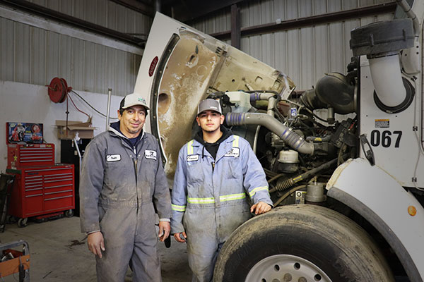 Mentor and student standing in front of a truck with the engine compartment open